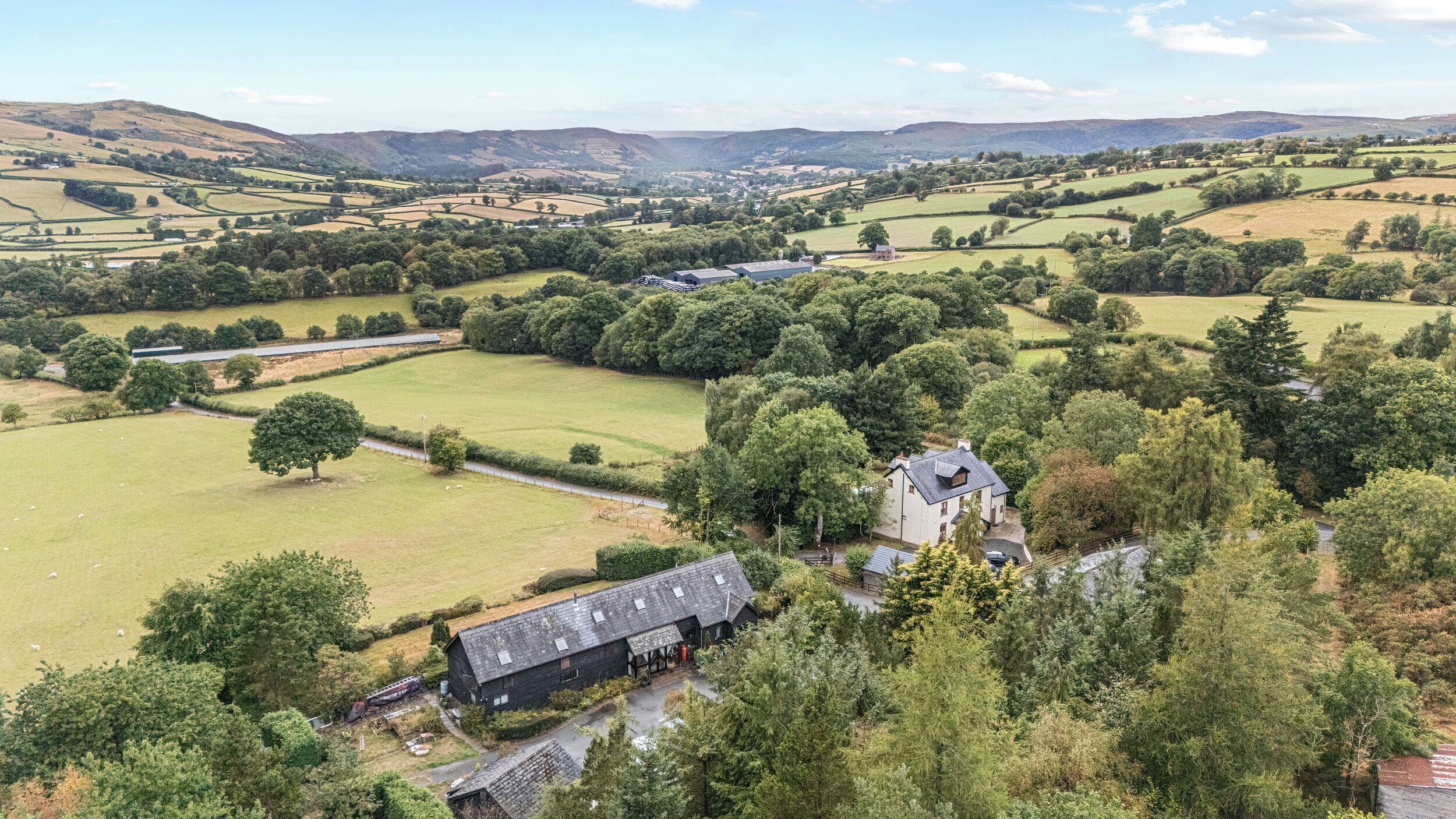 A rural landscape with rolling hills, a farmhouse, and scattered trees.