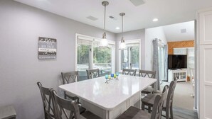 A modern dining area with a large table, multiple chairs, pendant lights, and a view of the outdoors. - Villa in Corolla Light with Views, Hot Tub & More! (Corolla)
