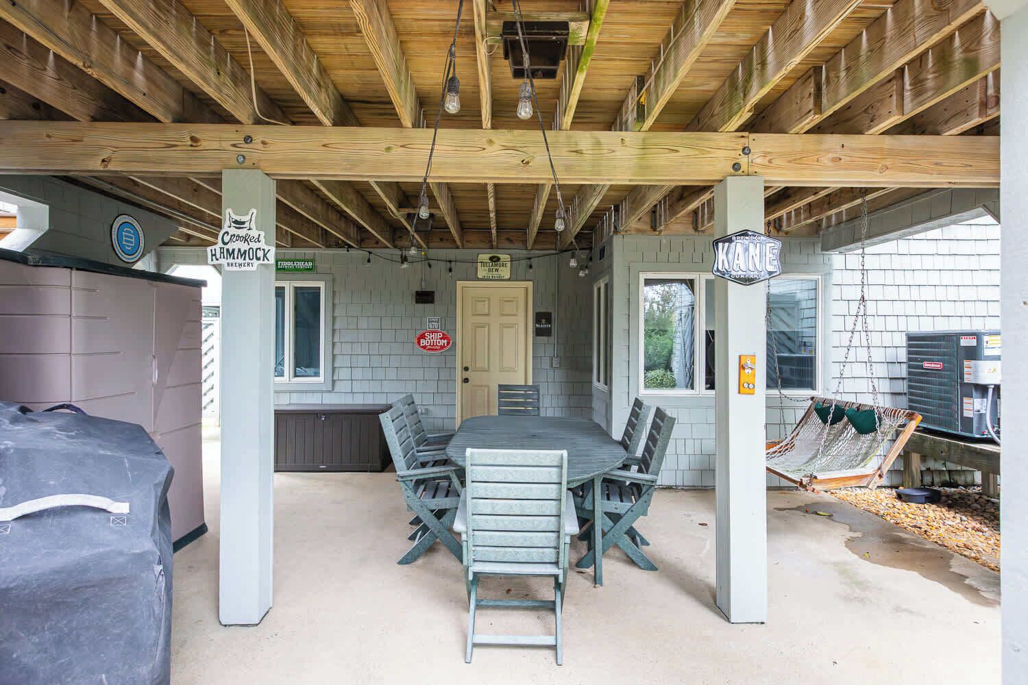 Een overdekt terras met een tafel, stoelen, een barbecue en een hangstoel.