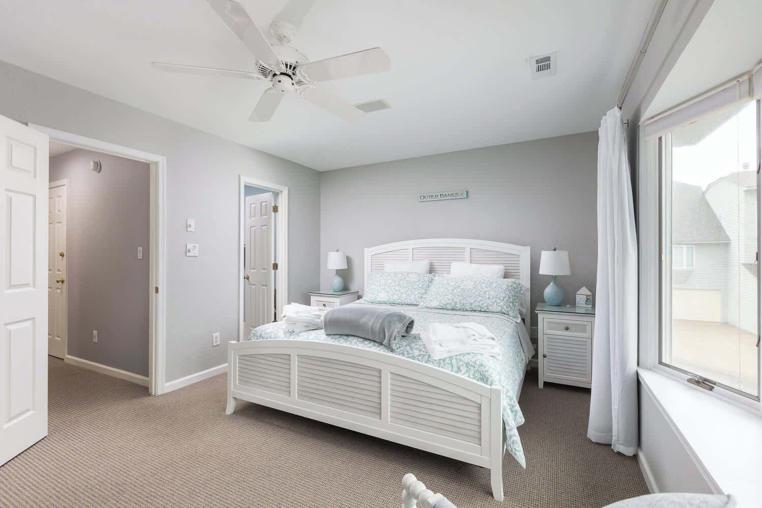 A bedroom with a white bed, two bedside tables, a ceiling fan, and a window with curtains.