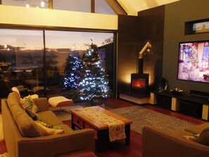 A cozy living room with a large window, a decorated Christmas tree, a fireplace, and a television. - Woodcroft (Pwllheli)