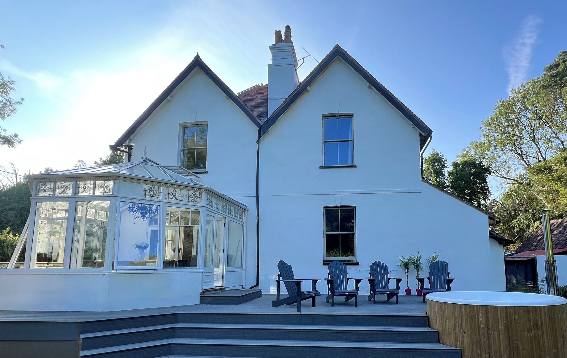A two-story house with a conservatory, a hot tub, and outdoor seating.