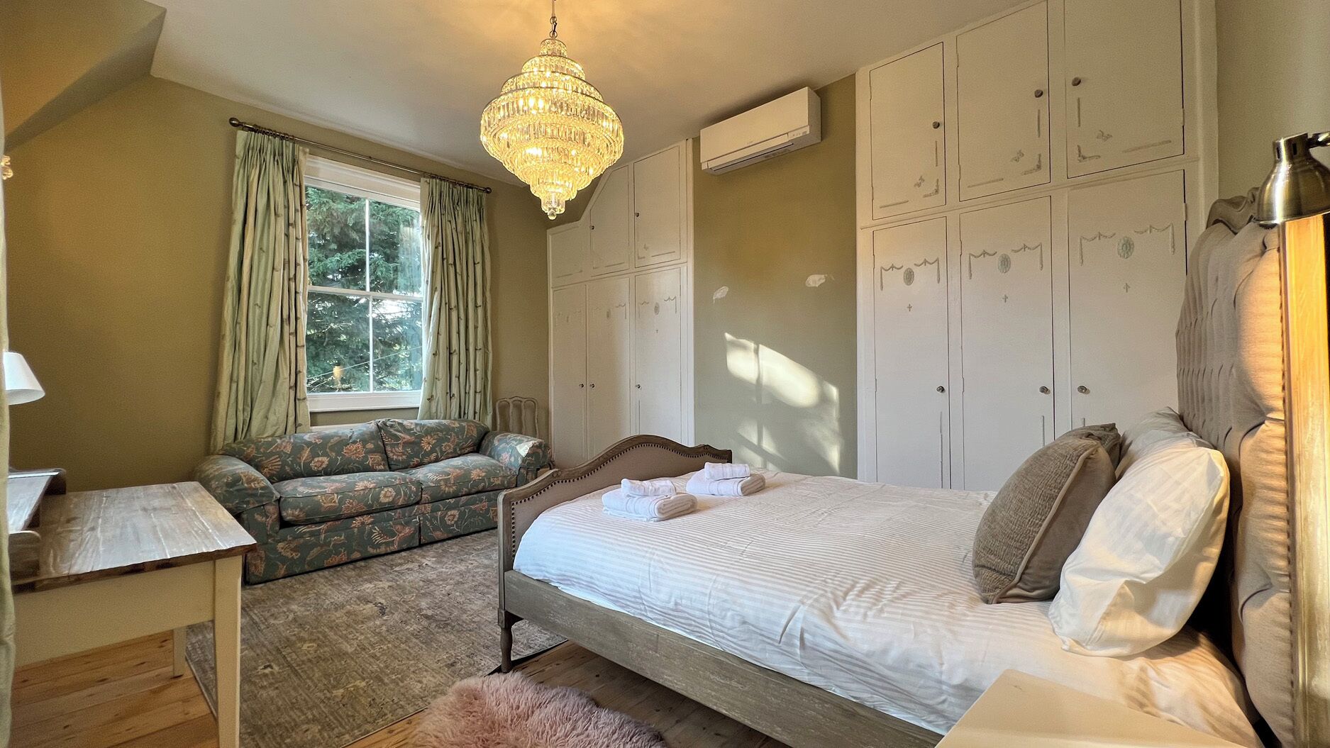 A bedroom with a bed, a sofa, a chandelier, and a wardrobe.