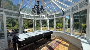A conservatory with a pool table, large windows, and a chandelier. - Your Country House (Reading)