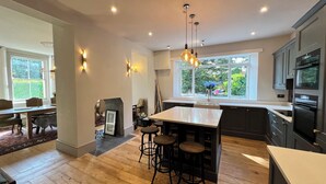 A modern kitchen with a central island, bar stools, and a large window providing a view of the outdoors. - Your Country House (Reading)