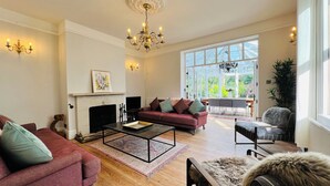 A spacious living room with a fireplace, a large window with a view of greenery, a chandelier, and a cozy seating area. - Your Country House (Reading)