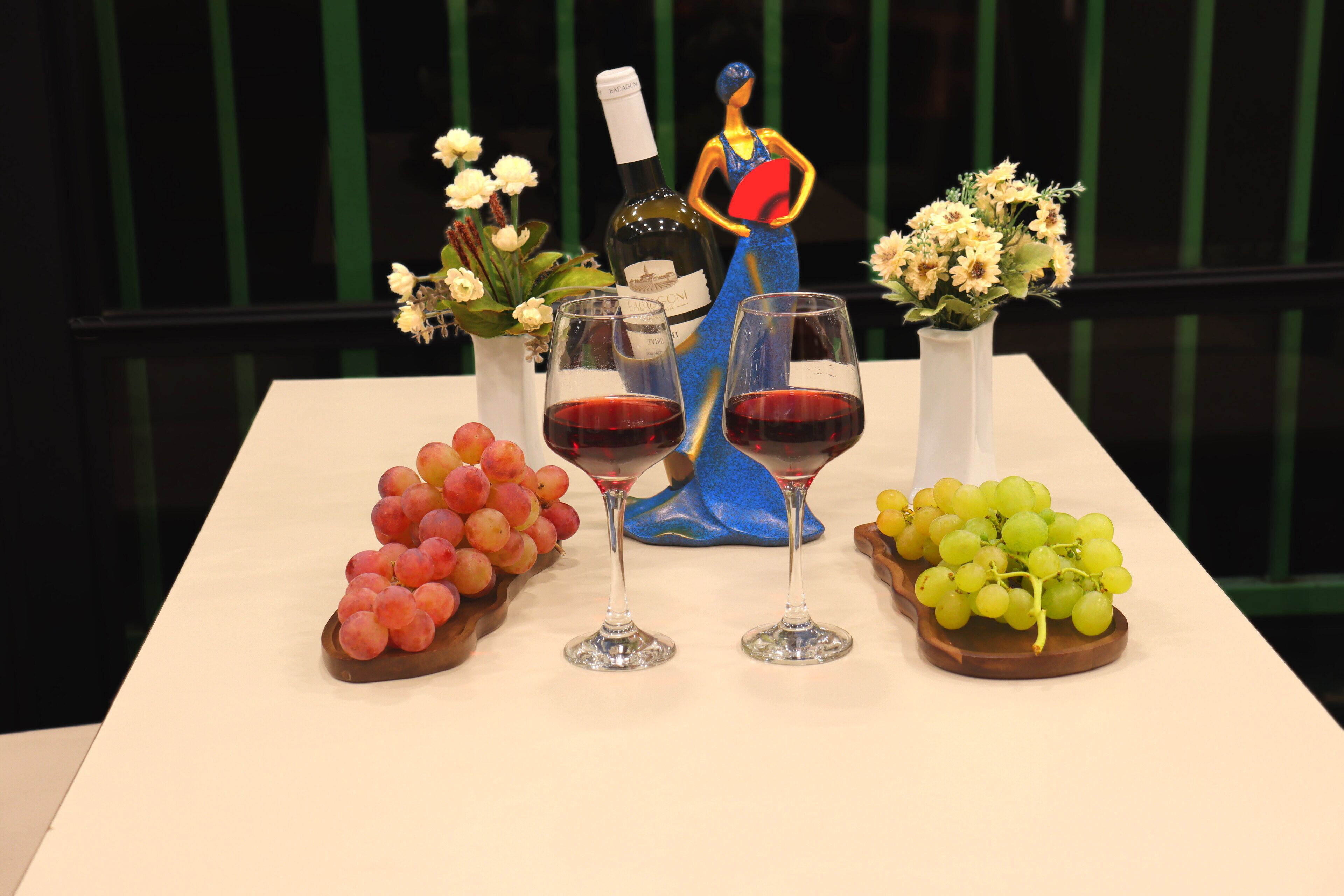 A table with two wine glasses, a bottle of wine, and decorative items including a figurine and flowers.