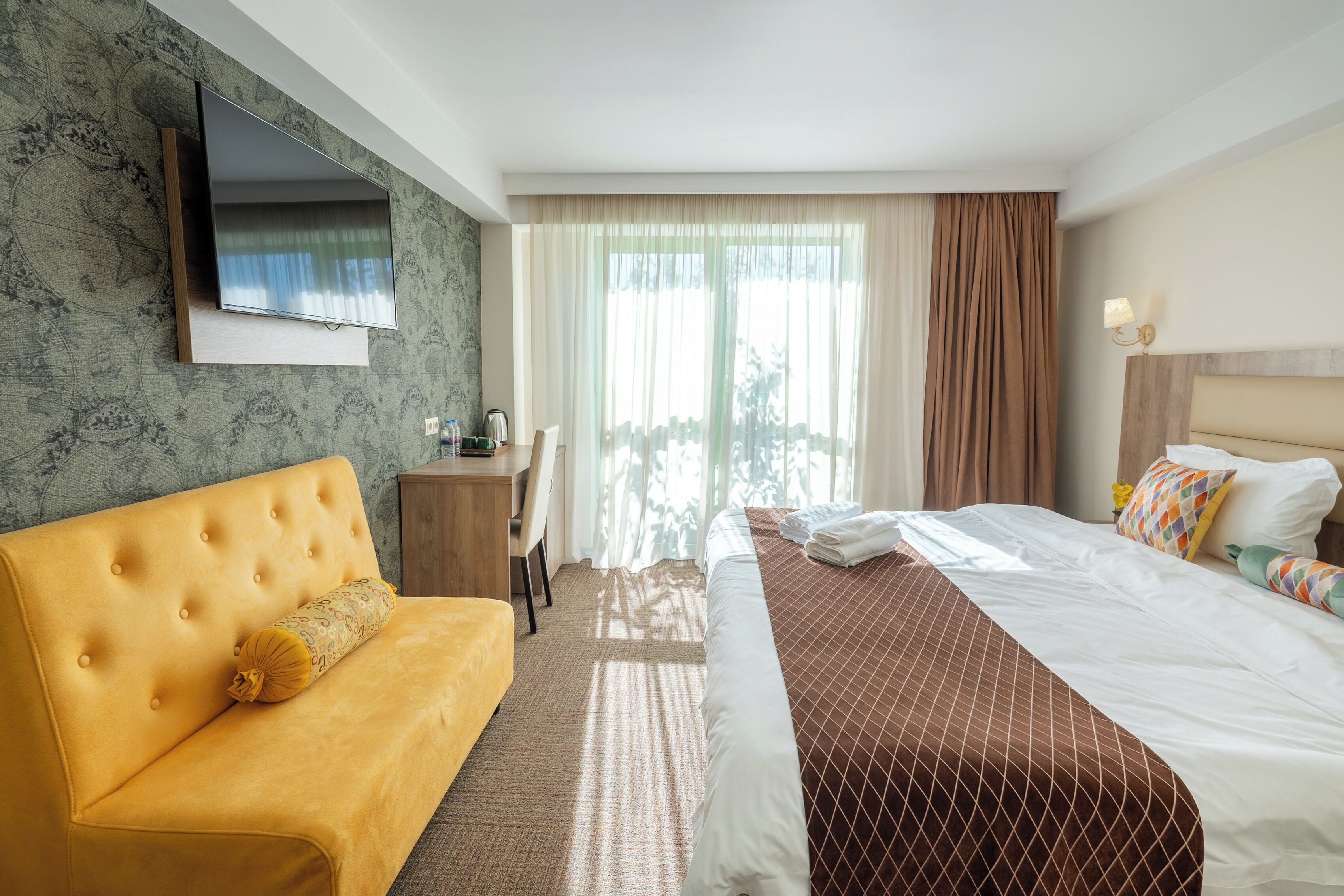 A hotel room with a sofa, a bed, a desk, and a TV mounted on the wall.