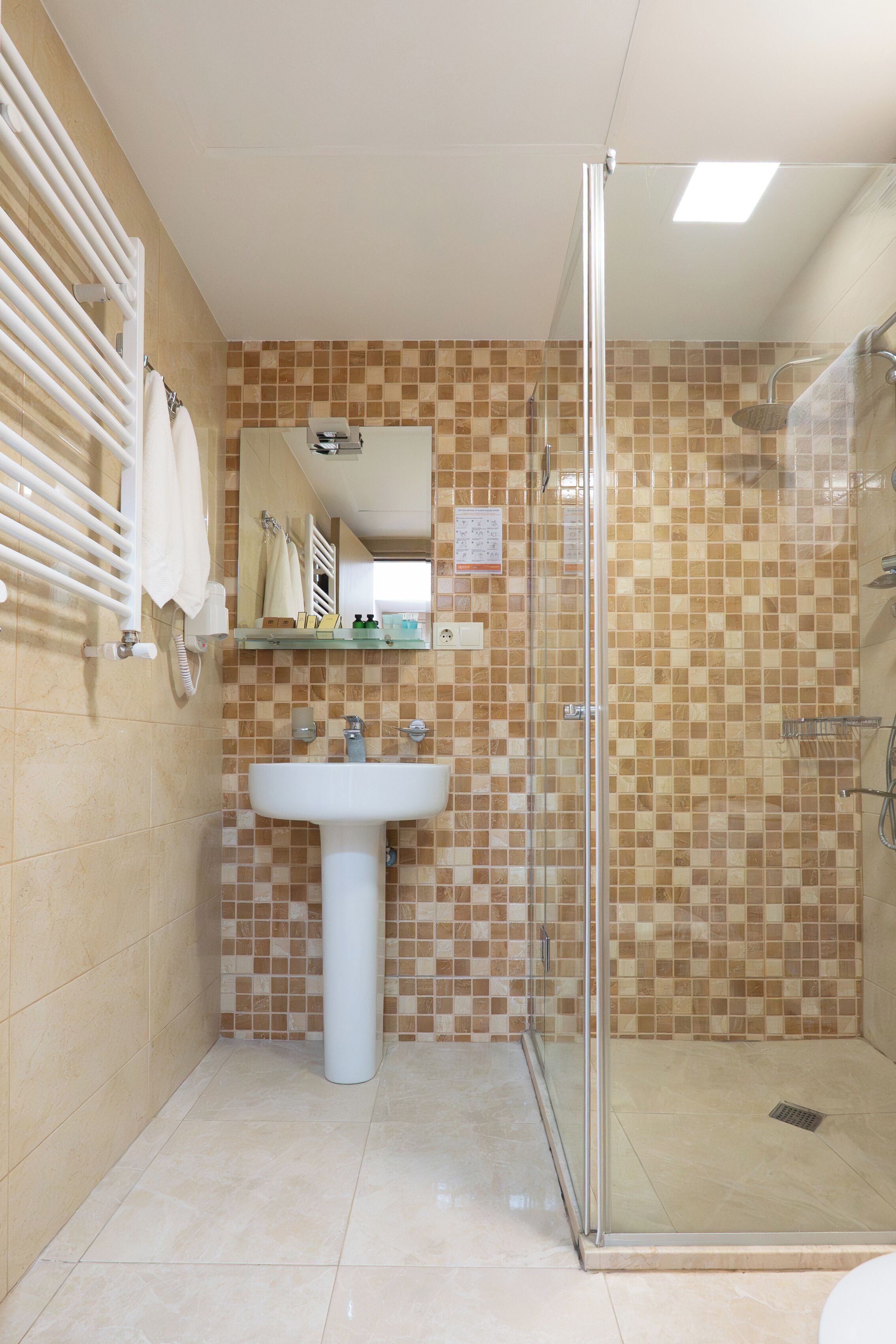 A bathroom with a glass-enclosed shower, a sink, and a tiled wall.