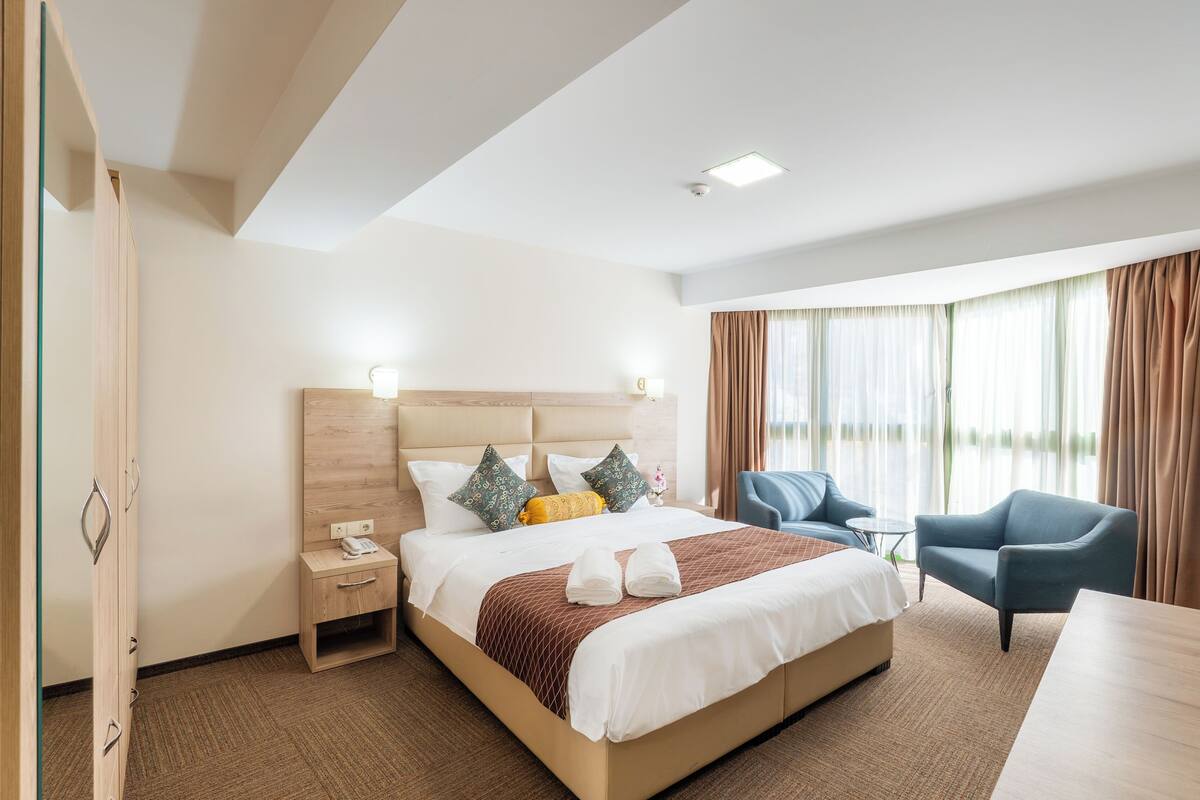 Una habitación de hotel con una cama grande, mesitas de noche, un escritorio y una silla.
