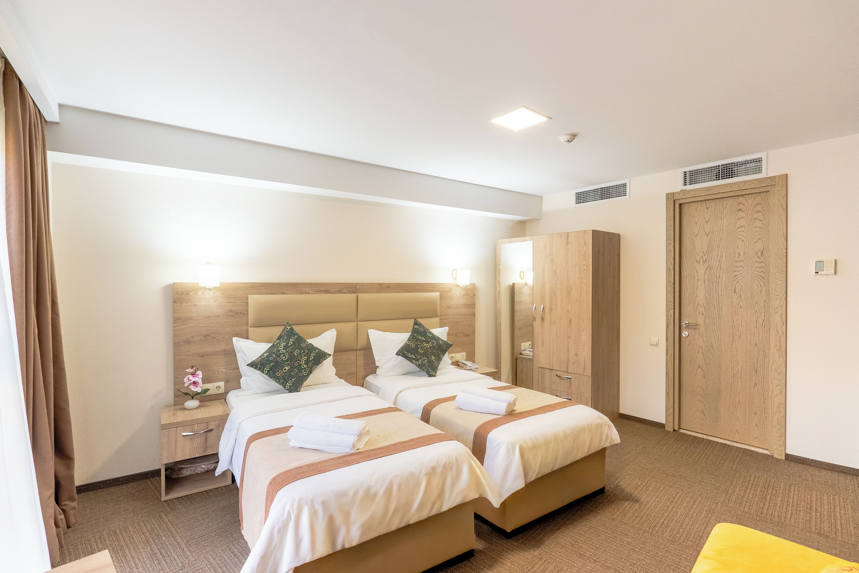 Una habitación de hotel con dos camas, un armario, una mesita de noche y una pequeña mesa con un jarrón de flores.