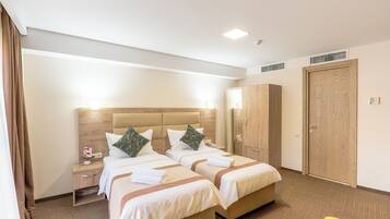Una habitación de hotel con dos camas, un armario, una mesita de noche y una pequeña mesa con un jarrón de flores.