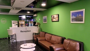 A reception area with a green wall, a reception desk, a brown leather sofa, and a marble coffee table. - Hotel Somi Inn (Tbilisi)