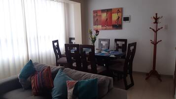 Una sala de estar con un sofá gris, una mesa de comedor con sillas, un cuadro en la pared y un perchero.
