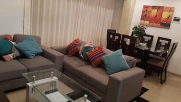 Una sala moderna con un conjunto de sofá, una mesa de centro de vidrio y un comedor con sillas y una mesa.