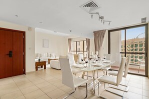 A modern dining area with a glass table, white chairs, and a view of the cityscape through large windows. - FIRST CLASS | 2BR | Spectacular Sea View (JBR)