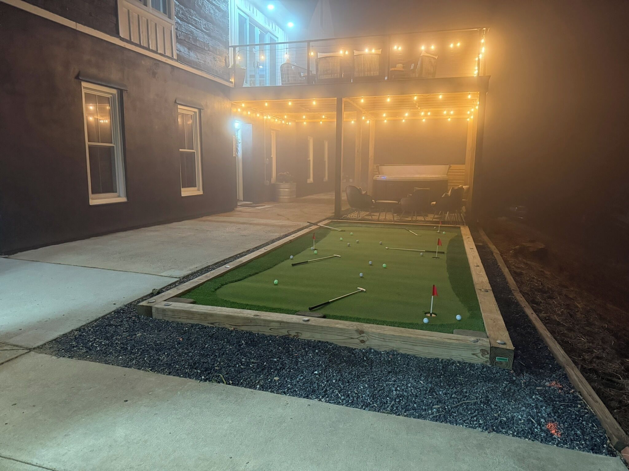 A backyard with a foosball table, a small pool table, and string lights.