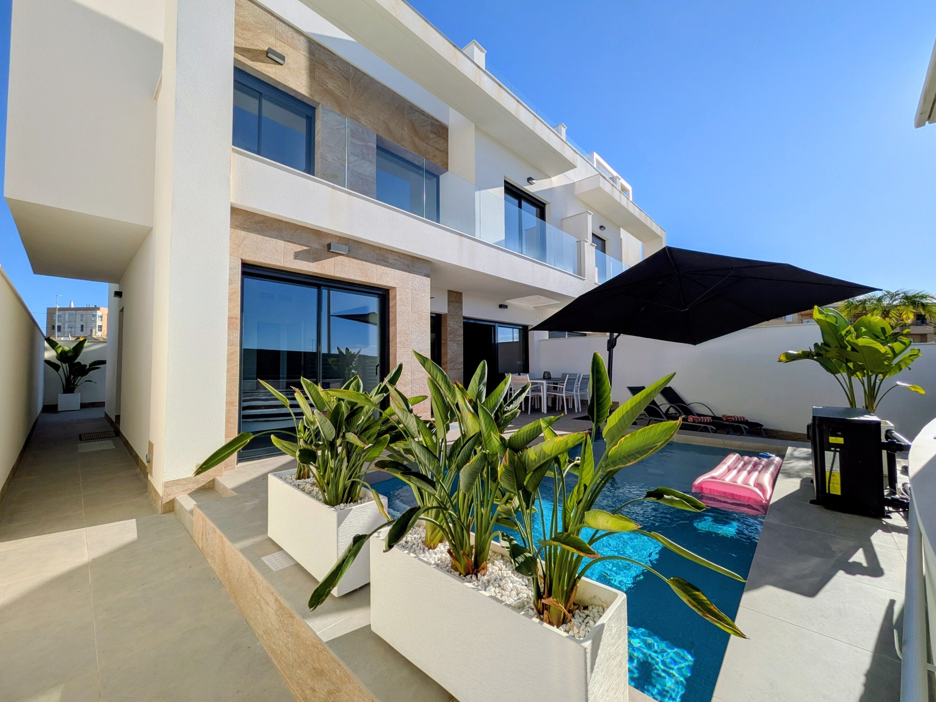 A modern two-story building with a swimming pool, outdoor seating, and potted plants.