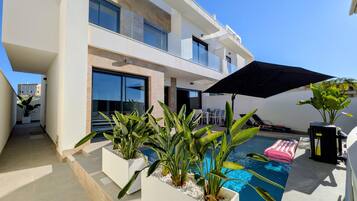 A modern two-story building with a swimming pool, outdoor seating, and potted plants.