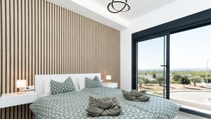 Moderni makuuhuone, jossa on suuri sänky, puinen säleverkkoseinä, yöpöytä lampun kanssa ja suuri ikkuna, josta avautuu näkymä maisemaan.