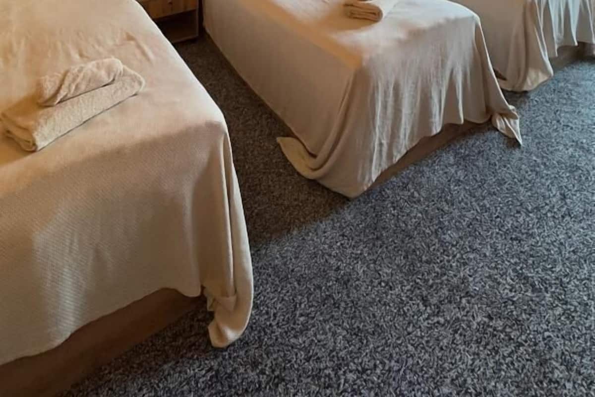 Habitación de hotel con tres camas individuales, techo de madera, un ventanal grande con cortinas y una lámpara en el techo.