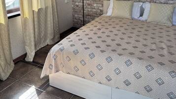Un dormitorio con pared de ladrillo visto, una cama con ropa de cama estampada, una lámpara de pie y una ventana con cortinas.