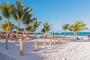 A beach with palm trees, a sandy path, and beach umbrellas. - Tropical Retreat / Pool / Fitness Center (Punta Cana)