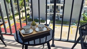 Un balcon avec une table dressée pour deux personnes, donnant sur un parking et des immeubles d’habitation.