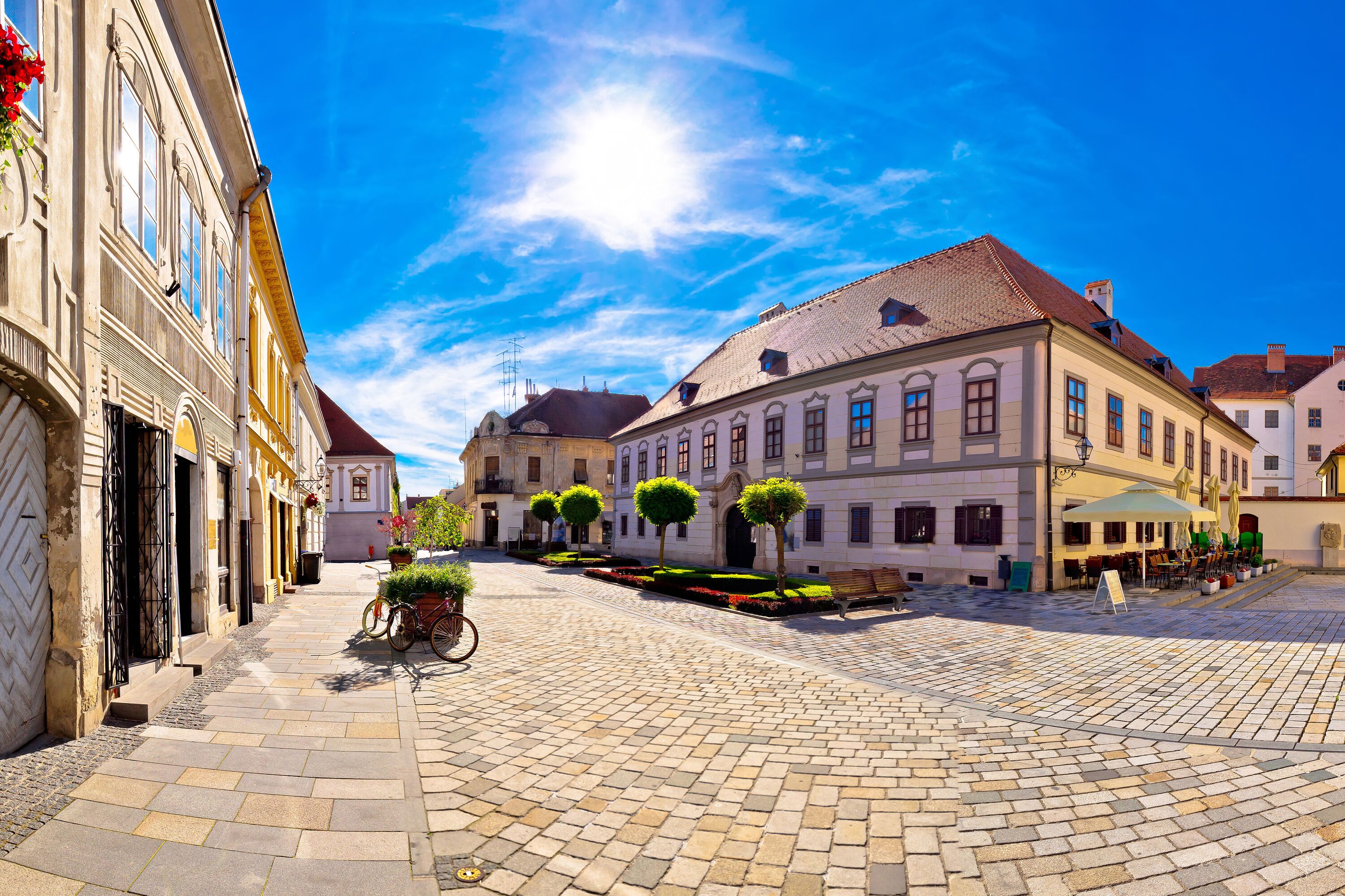 A cobblestone square with historic buildings, a bicycle, and a well-maintained garden.