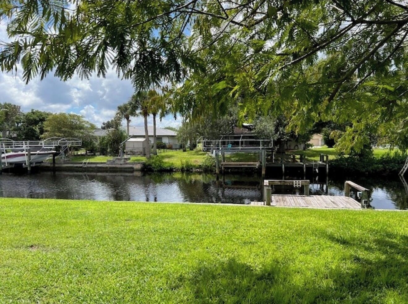 A tranquil riverside park with a wooden dock, a small bridge, and lush greenery.