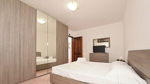 A bedroom with a large mirror, a bed with white bedding, a dresser, and a television. - Villa with a pool, Puglia – Libellule 3 (Carovigno)