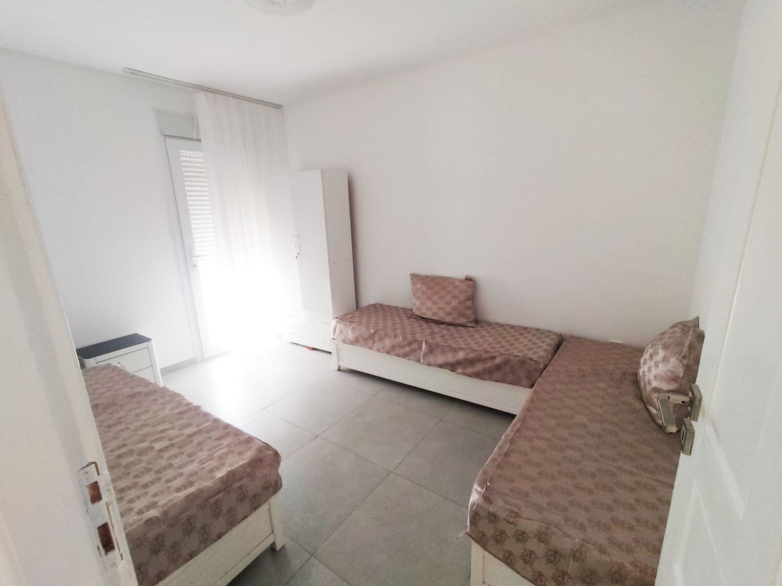 Una habitación pequeña y limpia con dos camas, un armario y una ventana con cortinas.