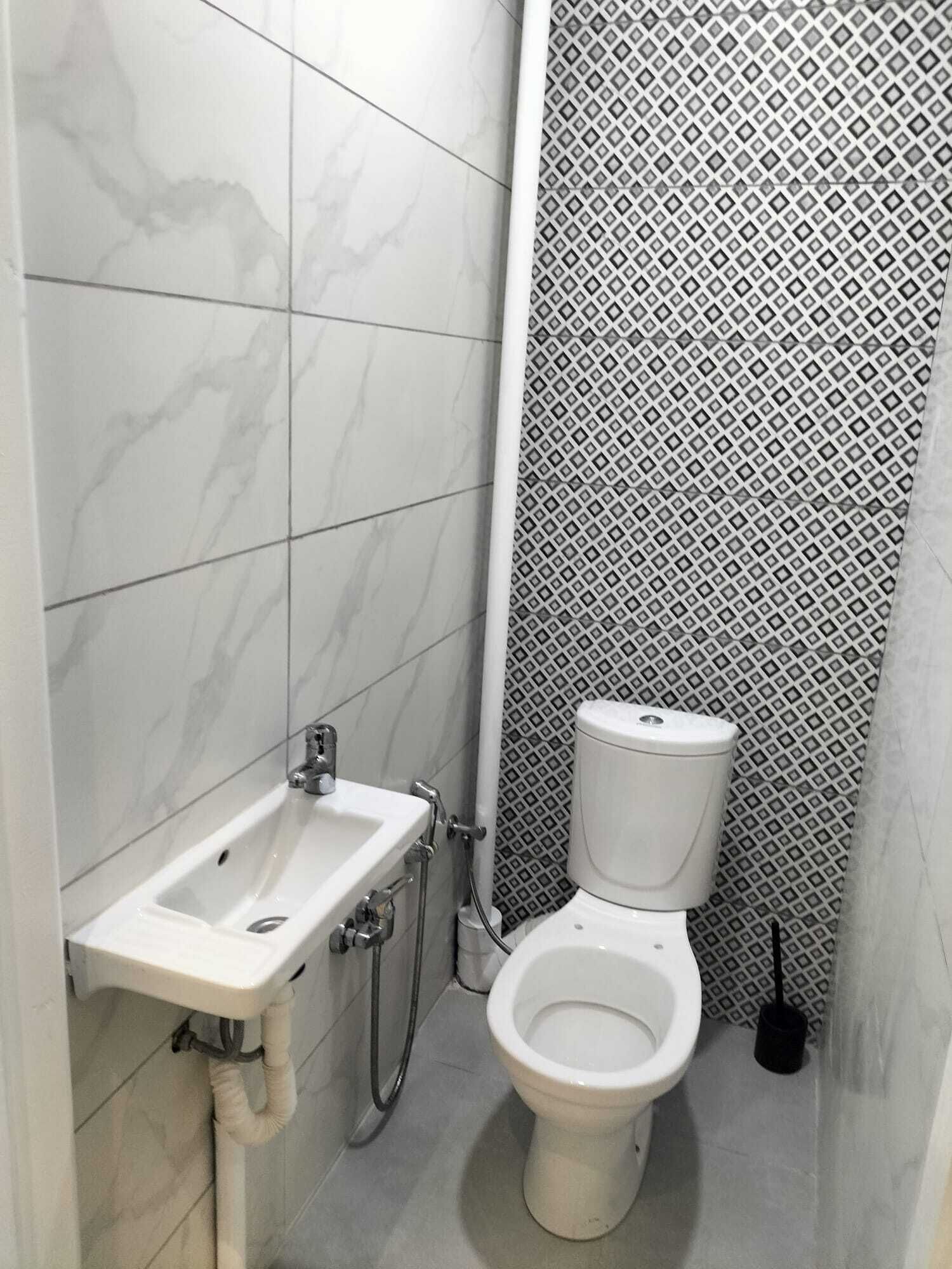 Et badeværelse med en hvid vask, toilet og brusebad. Væggene er beklædt med fliser i et marmor-mønster på den ene side og et geometrisk mønster på den anden.