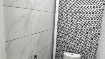 Et badeværelse med en hvid vask, toilet og brusebad. Væggene er beklædt med fliser i et marmor-mønster på den ene side og et geometrisk mønster på den anden.