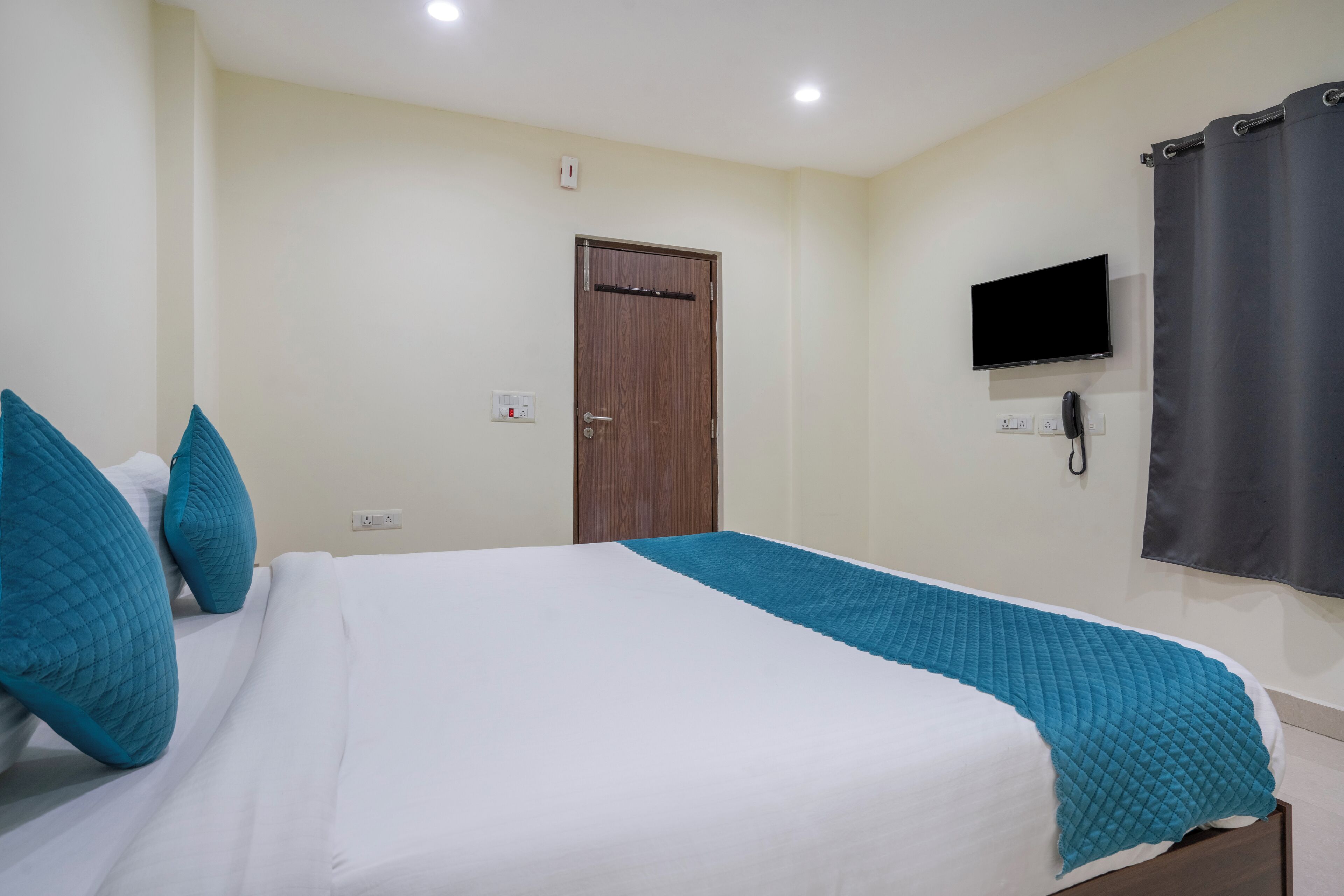 A hotel room with a bed, a TV mounted on the wall, and a door.
