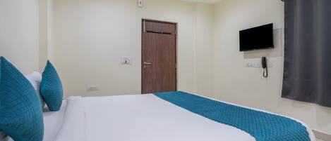 Une chambre d’hôtel avec un lit, un téléviseur fixé au mur et une porte.