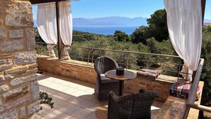 A stone-walled balcony with wicker furniture, a small round table, and a view of the sea and mountains. - Parenthèse enchantée dans une villa chic et élégante face à la mer (Kompi)