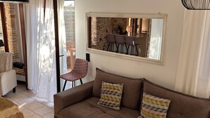 Un salon chaleureux avec un canapé marron, des coussins à motifs, un mur en pierre et un coin repas agrémenté d’un miroir au-dessus du bar.