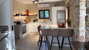 Une cuisine moderne avec des armoires blanches, un îlot central doté de tabourets de bar, un four encastré et un mur d’accent en pierre.
