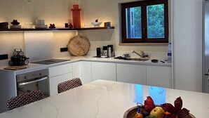 Une cuisine moderne dotée d’un îlot central, de meubles blancs et d’une fenêtre donnant sur un paysage verdoyant.