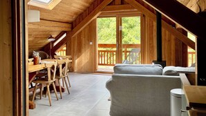 Ein geräumiges Loft mit hohen Decken, Holzbalken, einem Essbereich mit Tisch und Stühlen, einer Couch und Blick ins Freie.