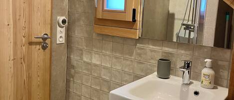A bathroom with a wooden door, a tiled wall, a small window, a sink with a mirror, and a green cabinet.