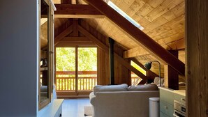 Ein geräumiges Dachzimmer mit Holzbalkendecke, einer Couch, einem Schreibtisch und einem Fenster mit Blick auf eine Terrasse.