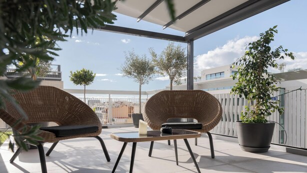 Un balcón con sillas de mimbre, una mesa y una planta en maceta.
