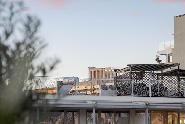 A rooftop terrace with a view of a cityscape, including a building with columns and a modern structure with a glass balcony. - Athens Golden Light Premium Residence, Bill & John Apartments & Villas (Athens)
