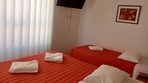 Habitació d'hotel amb dos llits, cadascun amb una mantella vermella i almoinos blancs. Hi ha un televisió de pantalla plana penjada a la paret sobre els llits.