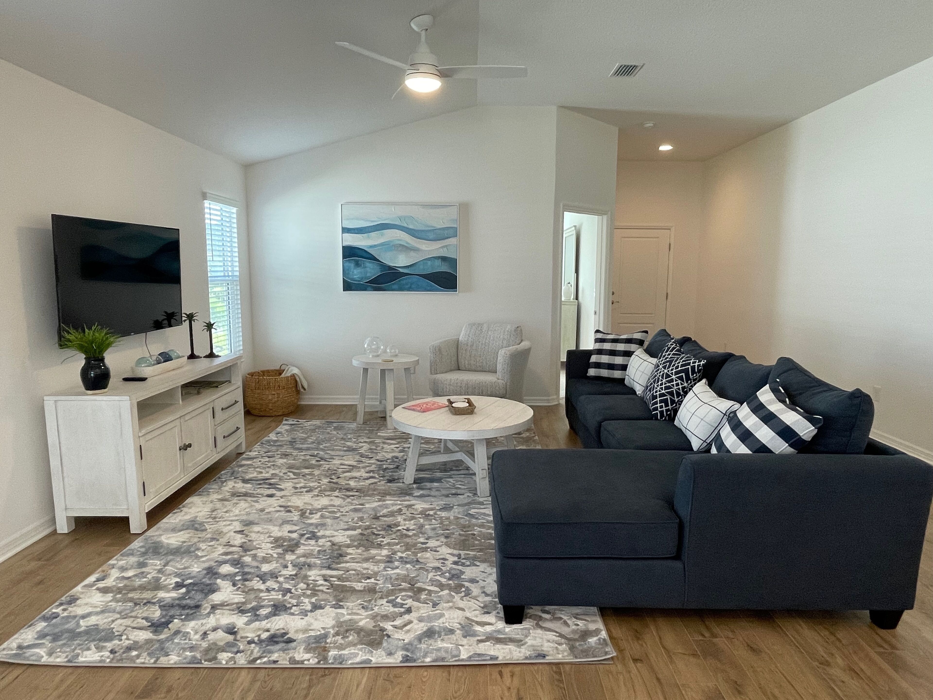 Una sala de estar moderna con un televisor de pantalla plana, un sofá gris, un sillón blanco y una mesa de centro.