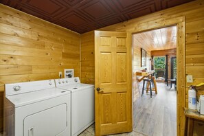 Innenansicht einer Holzhütte mit Waschbereich, einer Holztür und Blick auf einen Essbereich.