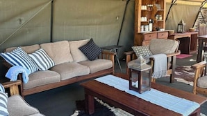 Alojamiento en tienda de campaña con sofá, sillones, mesa de madera y estantería.