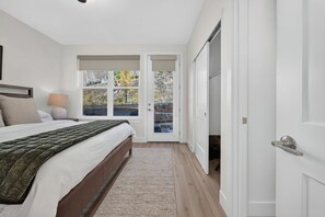 Et soveværelse med en seng, et natbord, en lampe og udsigt til det fri via en dør.